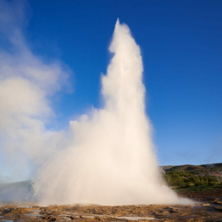 Eruption of the Geysir geyser. Valley Haukadalur, Iceland. Golden Ring Tourist Attraction. Sunny day with clear blue sky. Amazing nature