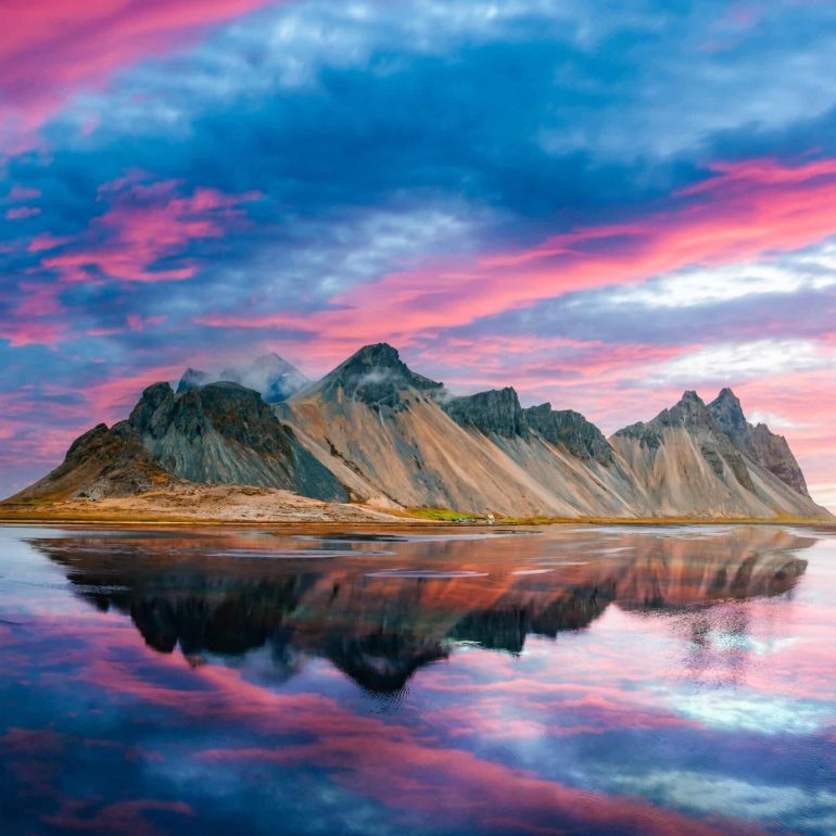 Mt. Vestrahorn on Stokknes Cape in southeastern Icelandic coast during sunset. The epic pink sky reflected in the clear water.