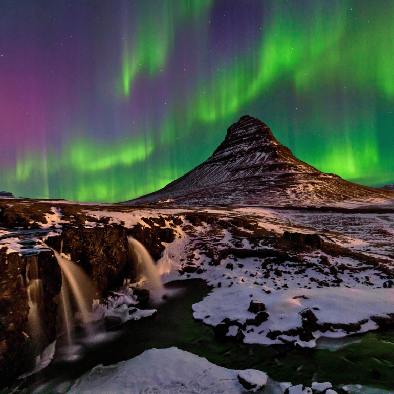 Northern lights dancing over snow-covered Mt. Kirkjufell on Iceland's Snæfellsnes Peninsula, waterfall in the foreground.