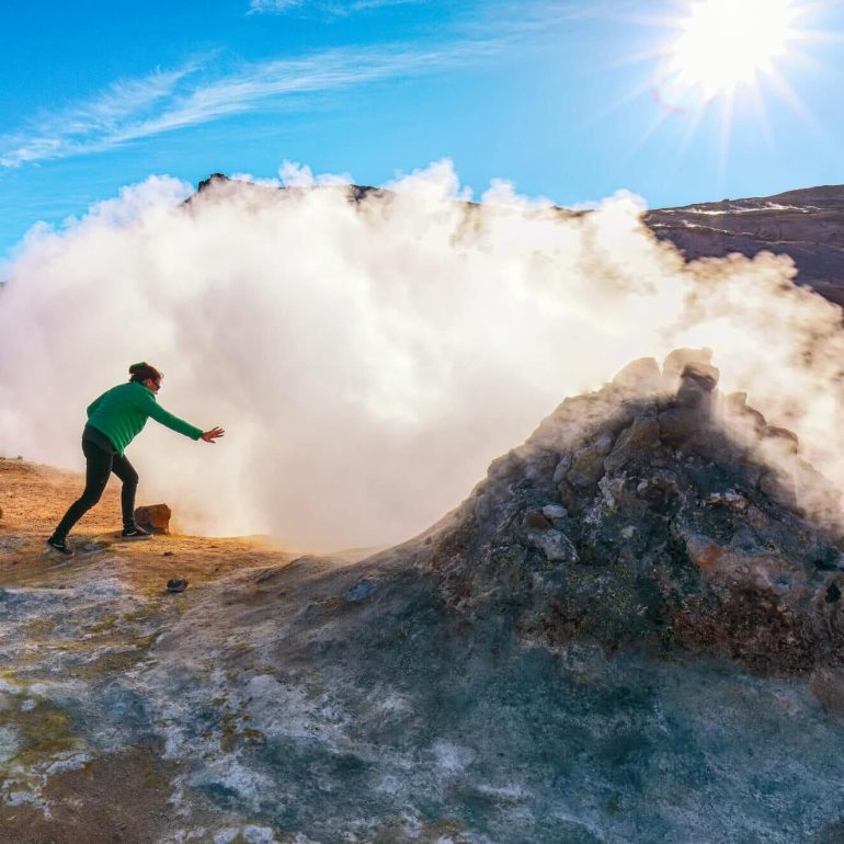 A man standing in front of a steaming fumarol in Hverir Geothermal Region in the Lake Myvatn Area, North Iceland.