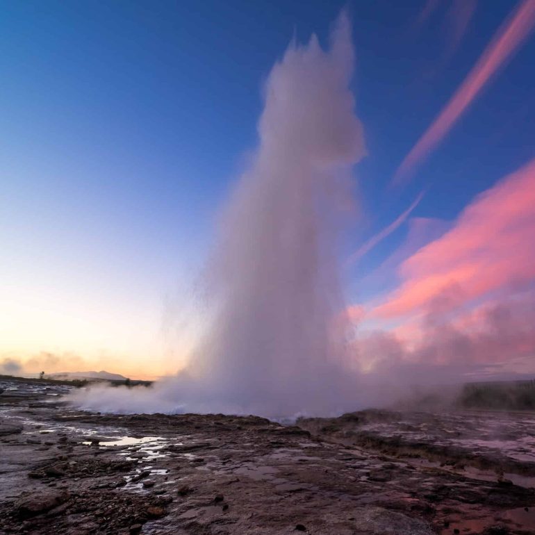 Strokkur geyser erupting on Iceland's Golden Circle route, pink skies.