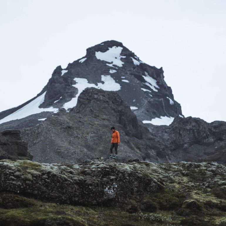 Un randonneur devant un sommet enneigé, entouré de paysages volcaniques dans le sud de l'Islande.