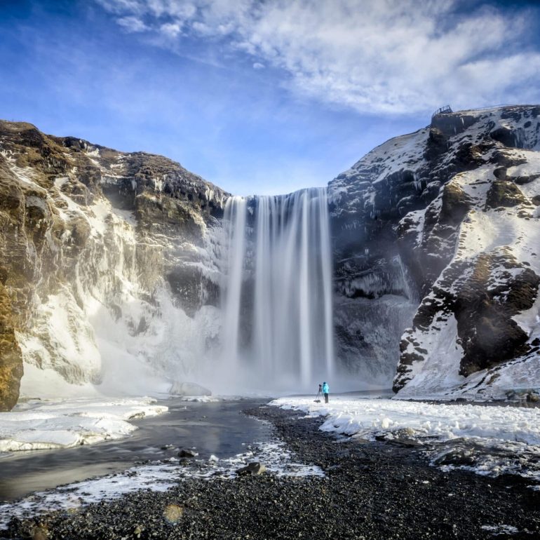 Skógafoss Waterfall in South Iceland in the winter, blue sky and snowy cliffs.